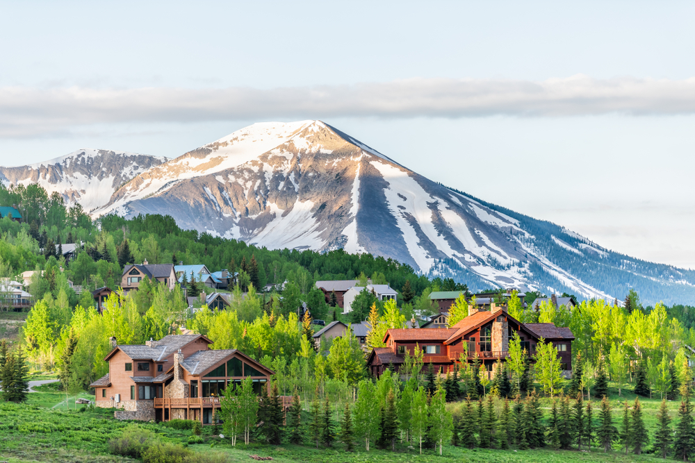 Mount Crested Butte, Colorado village in summer with colorful sunrise by wooden lodging houses on hills with green trees